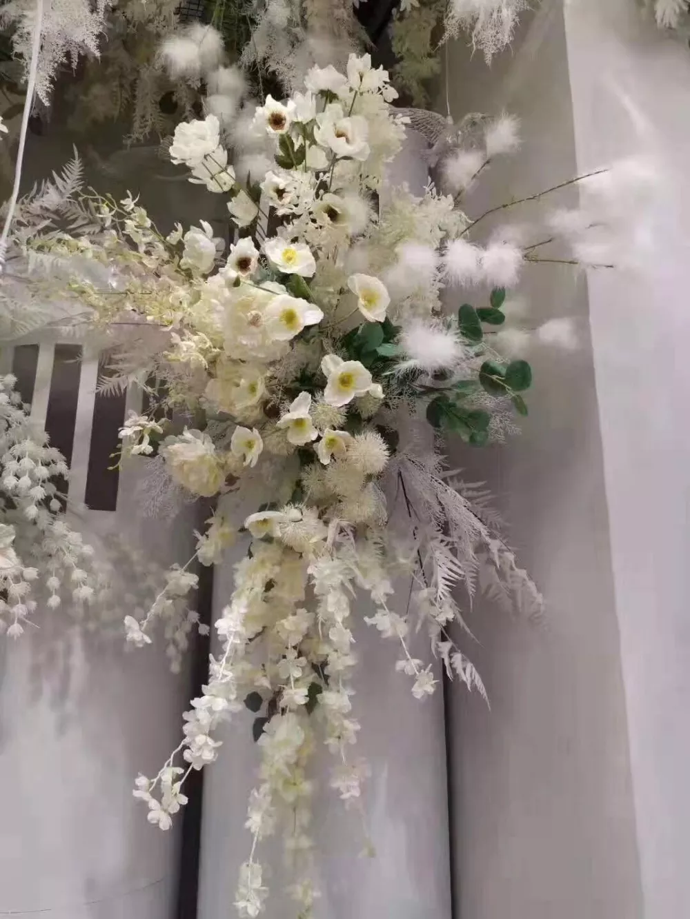 Full white wedding theme featuring artificial flower balls, arch, and flower wall